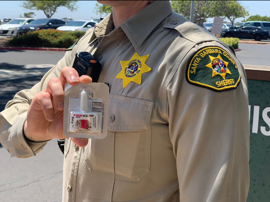 Police officer holding a Narcan nasal spray, demonstrating its use in a private jail setting as part of affordable options for overdose prevention and safety.